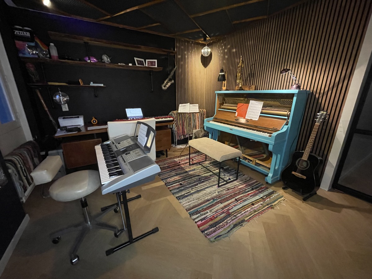 Overzicht van de lesruimte met piano, keyboards en houten wanden